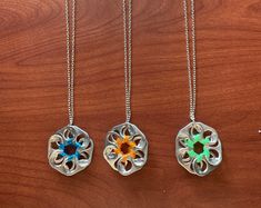 three necklaces with different designs on them sitting on top of a wooden table next to each other