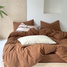 an unmade bed with brown sheets and pillows on top of it in front of a wooden headboard