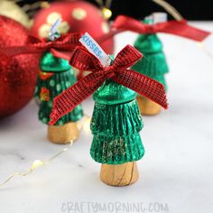 three small green christmas trees with red bows and ornaments behind them on a white surface