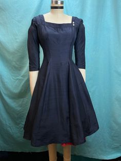 "1950s W:26 Deep ink navy silk shantung dress with square neckline rhinestones back drape circle skirt fit and flare Vintage 50s beautiful silk shantung dress. Deep ink navy color with square neck adorned with two rhinestone flowers, 3/4 sleeveless. Exquisite back drape attached to center back covering zipper with a cream border. Paneled circle skirt silhouette. Unlined. Added red petticoat not included.  MEASUREMENTS  Bust: 34\" Waist: 26\" Hips: free Bodice length: 14\" Skirt length: 25\" with no hem available to let down This is in overall in good vintage condition, there's a couple of pinholes and pulls and stress to the fabric. The drape has some shattering to the silk as pictured. This still presents beautifully and is completely wearable as is! ✨" Fitted Satin Dress With Box Pleat Details, Fitted Satin Dress With Box Pleat, Vintage A-line Cocktail Dress With Fitted Bodice, Fitted Silk Dress With Box Pleat, Fitted Silk Dresses With Box Pleat, Silk A-line Dress With Box Pleat, Silk Square Neck Dresses For Formal Occasions, Formal Silk Dress With Square Neck, Formal Silk Square Neck Dress