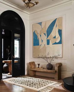 a large painting hangs on the wall next to a wooden bench in front of a black door