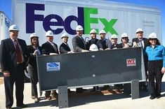 a group of men and women standing in front of a fed ex truck with hard hats on