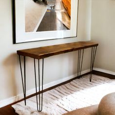 a wooden table with hairpin legs in front of a framed photograph on the wall