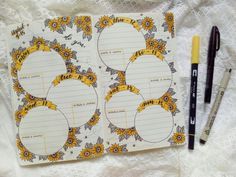 an open notebook with sunflowers on it next to two markers and a pen