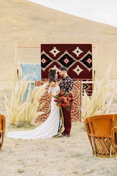 a couple standing in the middle of a field next to some chairs and rugs