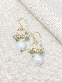 These handcrafted earrings feature radiant gold circles embellished with lustrous white baroque pearls and delicate clusters of tiny green gemstones and pearls. Enjoy an artistic bohemian vibe while adding an elegant and timeless touch to any ensemble. MATERIALS ~ Baroque pearls ~ Freshwater seed pearls ~ Green kyanite ~ Prehnite ~ Crystal quartz ~ Vermeil circles ~ Gold-filled ear wires ~ Gold-filled head pins MEASUREMENTS ~ Earring drop is 1.5 inches from the top of the ear wire ~ Circles are Gold Pearl Earrings With Natural Stones, Bohemian Green Jewelry With Pearl Charm, Gold Pearl Drop Earrings For May Birthstone, Bohemian Gold Beaded Pearl Earrings, Green Dangle Pearl Earrings, Green Drop Earrings With Pearl Charm, Gold Bohemian Pearl Earrings With Dangling Beads, Bohemian Gold Pearl Earrings With Dangling Beads, Green Pearl Dangle Earrings