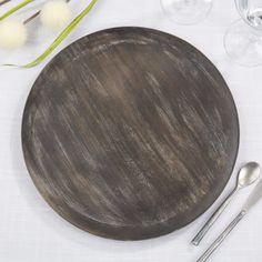 a wooden plate sitting on top of a table next to wine glasses and utensils