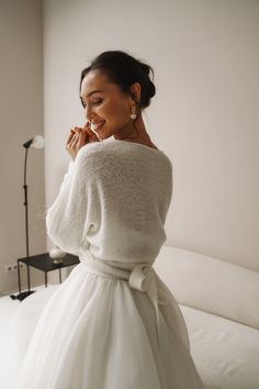 a woman in a white dress is talking on her cell phone while standing next to a bed