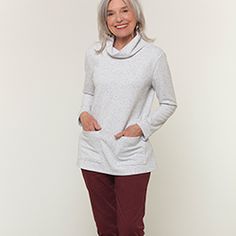 an older woman standing in front of a white wall wearing red pants and a gray sweater