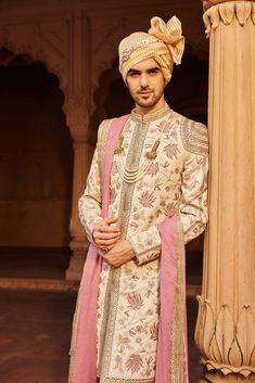 A heavily hand-embellished sherwani featuring intricate geometric and floral patterns, paired with a kurta, pants, and an embroidered stole draped elegantly over the shoulder. Luxury Pink Sherwani For Transitional Season, Eid Raw Silk Sherwani With Intricate Embroidery, Eid Sherwani With Intricate Embroidery In Raw Silk, Bollywood Style Raw Silk Sherwani With Intricate Embroidery, Reception Sherwani With Dabka Work, Bollywood Style Sherwani With Intricate Embroidery In Raw Silk, Embroidered Jamawar Sherwani With Traditional Drape, Raw Silk Sherwani With Dabka Work, Festive Sherwani With Intricate Embroidery On Straight Kurta