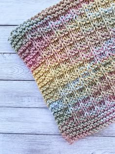 a crocheted dishcloth is laying on a white wooden surface with a blue and yellow stripe