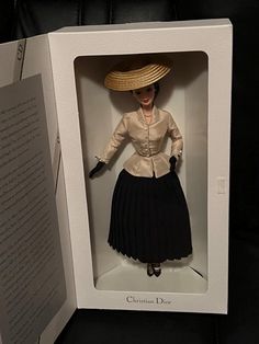 a doll in a white box with a black skirt and hat on it's head