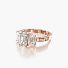 an engagement ring with two emeralds and diamonds on the sides, set in 18k rose gold