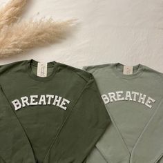 two sweatshirts with the words breathe and breathe on them next to some dried grass