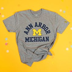 Rock your Ann Arbor pride with our exclusive Ann Arbor x Michigan Tee! This tee features a classic U of M vibe that perfectly captures the spirit of the U. Whether you're strolling through the Diag or grabbing coffee on Main Street, this tee is your go-to for showing off your hometown love in style. Super soft stonewashed tri-blend poly/cotton/rayon (50/25/25).Designed in Michigan by The Mitten State.Assembled in USA.Officially licensed by the University of Michigan. Casual T-shirt With Lettering For Game Day, Casual T-shirt With Lettering For Fans, Game Day Relaxed Fit T-shirt With Lettering, Relaxed Fit T-shirt With Lettering For Game Day, Collegiate Cotton T-shirt With Lettering, Fan Merchandise Relaxed Fit T-shirt With Lettering, Casual Tops With Fan Gear Lettering, Casual Tops With Lettering For Fan Gear, Graphic Tee With Lettering For Game Day