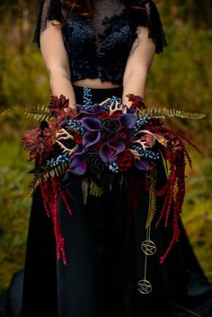 a woman in a black dress holding a bouquet with red and purple flowers on it