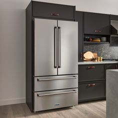 a stainless steel refrigerator in a kitchen with black cabinets and wood flooring on the walls