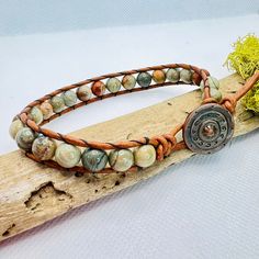 a leather bracelet with beads and metal clasps on a piece of wood next to a plant