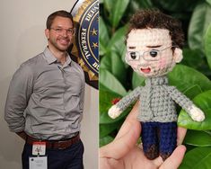 a man standing next to a hand holding a crocheted doll in front of him