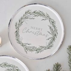 two plates decorated with greenery and the words merry christmas written in silver on them