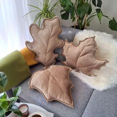 three leaf shaped pillows sitting on top of a couch next to a potted plant