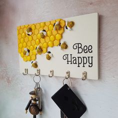 two key chains hanging from hooks on a wall next to a sign that says bee happy