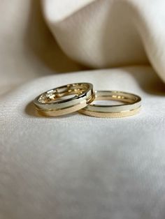 two gold wedding rings sitting on top of a white cloth covered bed sheet, close up