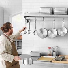 a man in an apron is hanging pots and pans on the wall