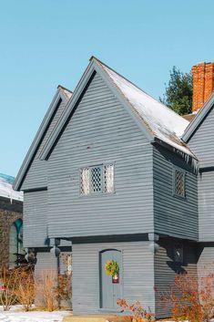 an old gray house with snow on the ground and trees in the backgroud