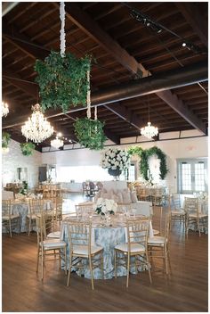 a room filled with lots of tables and chairs covered in white tablecloths under chandeliers