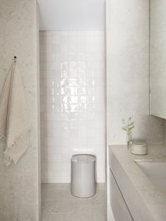 a bathroom with white tile walls and flooring, along with a trash can in the corner