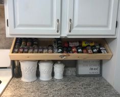 an organized spice rack in a kitchen with white cabinets and granite counter tops, along with spices on the bottom shelf