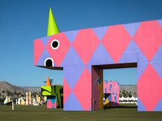 a large pink and purple building with a green hat on it's head in the middle of a field