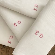 three white napkins with embroidered letters on them sitting on a wooden table next to each other