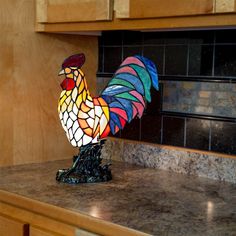 a stained glass rooster lamp sitting on top of a kitchen counter next to a wooden cabinet