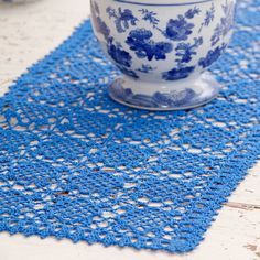 a blue and white doily on a table with a cup in the middle next to it