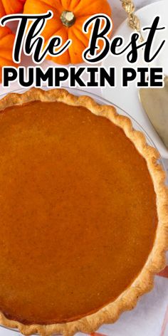 a pumpkin pie sitting on top of a table next to a white plate and orange pumpkins