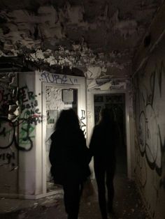 two people walking down an alley way with graffiti all over the walls and door frames