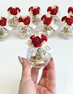 a hand is holding a small glass vase with flowers in it, and there are many smaller ones on the table