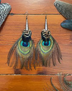 two peacock feathers are hanging from hooks on a wooden surface