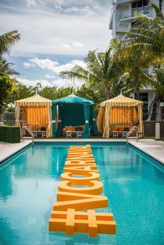 an outdoor swimming pool with chairs and umbrellas in the background, next to a large sign that says love