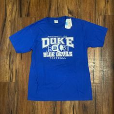 a t - shirt that says duke blue devils on the front, and is laying on a wooden floor