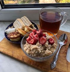 a bowl of oatmeal with strawberries on top next to a cup of tea