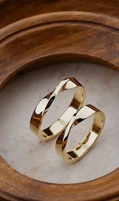 two gold wedding rings sitting on top of a wooden frame