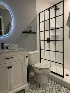 a white toilet sitting in a bathroom next to a walk in shower and sink under a mirror