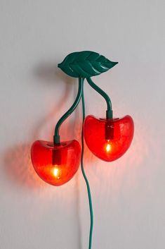 two red heart shaped lights are attached to a white wall with green leaves on them