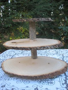 two tiered wooden cake stand on top of a white tablecloth with trees in the background