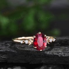 a close up view of a ring with a red stone and two diamonds on it