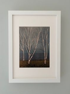 a white frame holds a painting of trees in the distance, against a gray wall