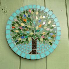 a mosaic tree on the side of a green wooden wall with blue and white tiles